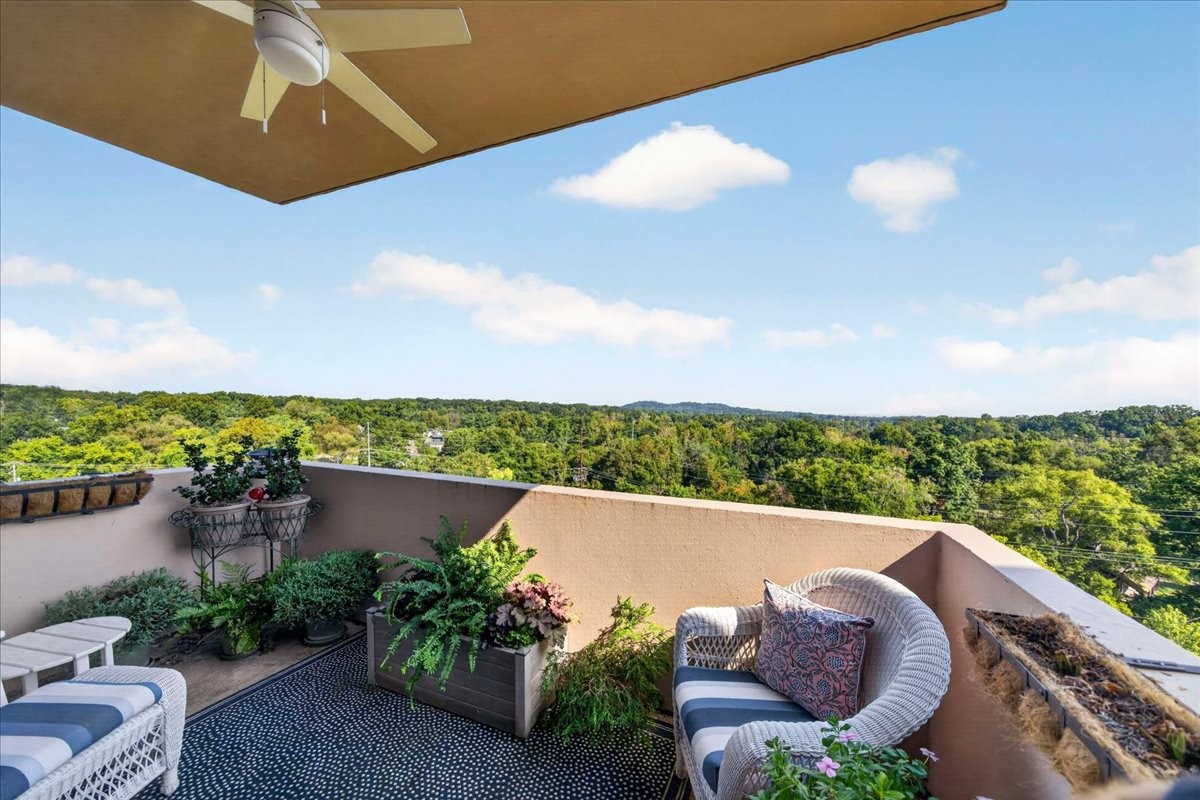 Furnished terrace with wicker seating and potted plants overlooking wooded hills.