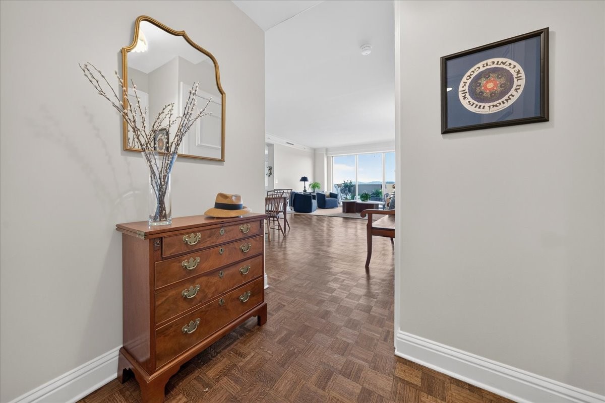 Condo entryway with parquet flooring and an antique dresser, opening into a bright living and dining area.