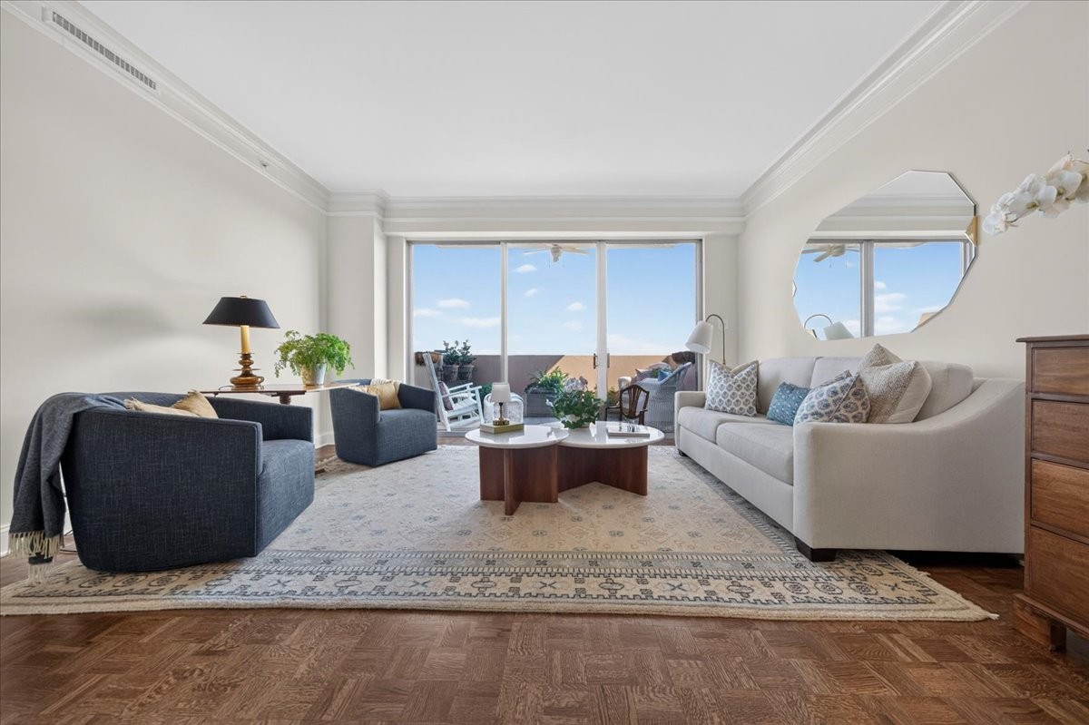 Furnished living room with blue armchairs, a white sofa, and glass doors opening to a balcony.