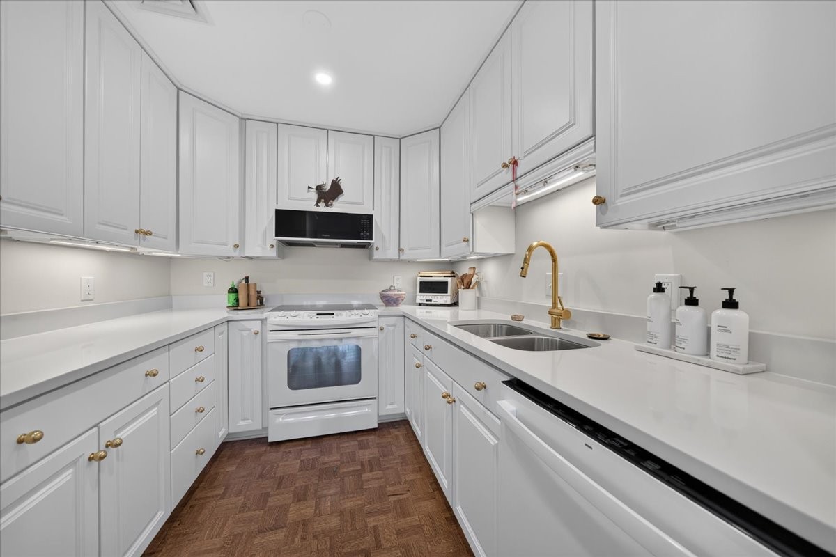 White kitchen with paneled cabinets, a brass faucet, and brown parquet flooring.
