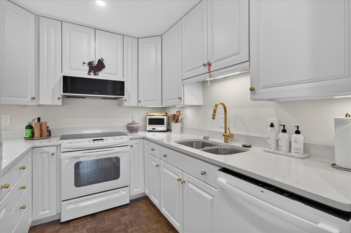 Kitchen with white cabinetry and countertops, a white range, and a double sink with brass faucet.