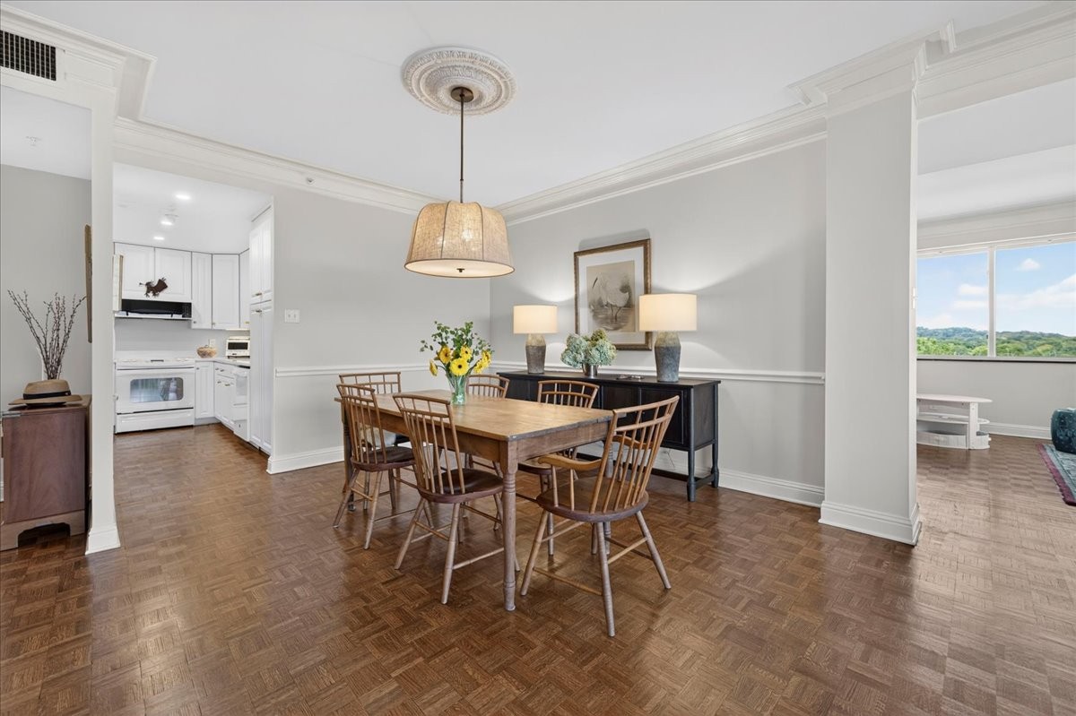 Dining room with a wooden table, parquet floors, and a view of green hills.