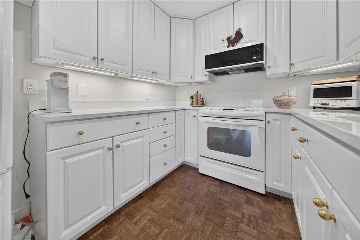 Kitchen with white cabinets and appliances and a brown parquet floor.
