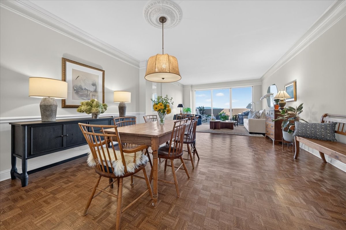 Open-plan dining and living room with parquet floors, a wooden dining table, and large windows.