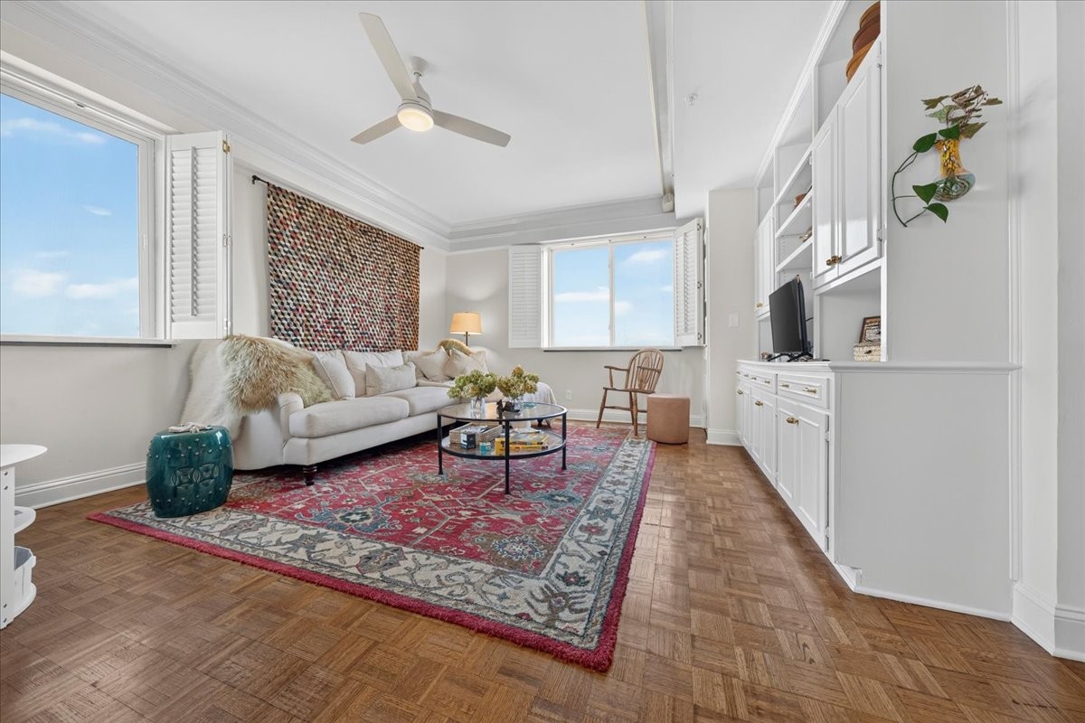 Living room with a white sofa, built-in cabinetry, open windows, and a colorful rug over parquet flooring.