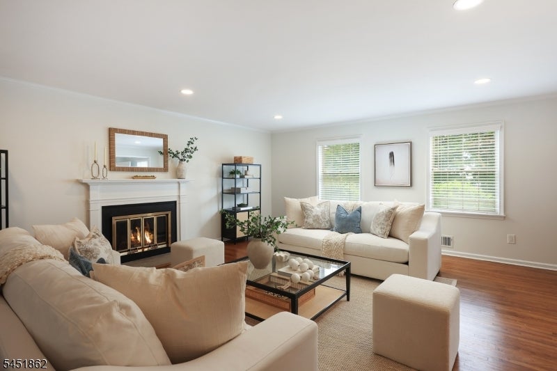 Living room with cream seating, a lit fireplace, hardwood floors, and two bright windows.