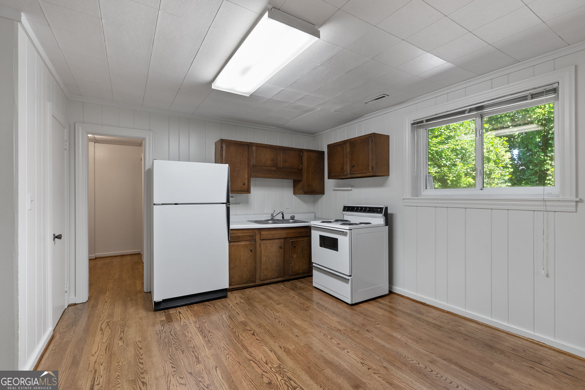 Kitchen with dark wood cabinets, white appliances, hardwood floors, and a large window overlooking greenery.