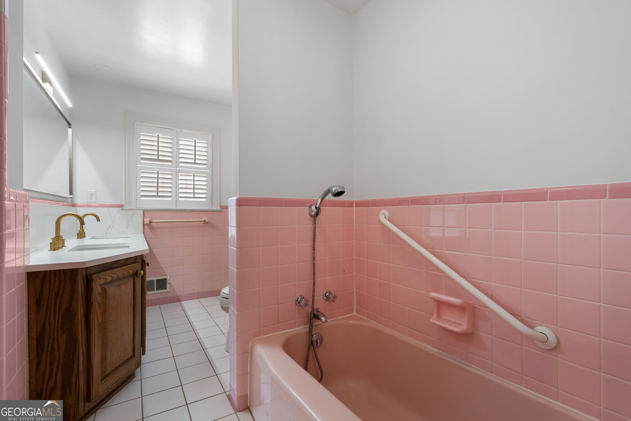 Bathroom with pink tile, a bathtub and shower grab bar, and a dark wood vanity with brass faucets.