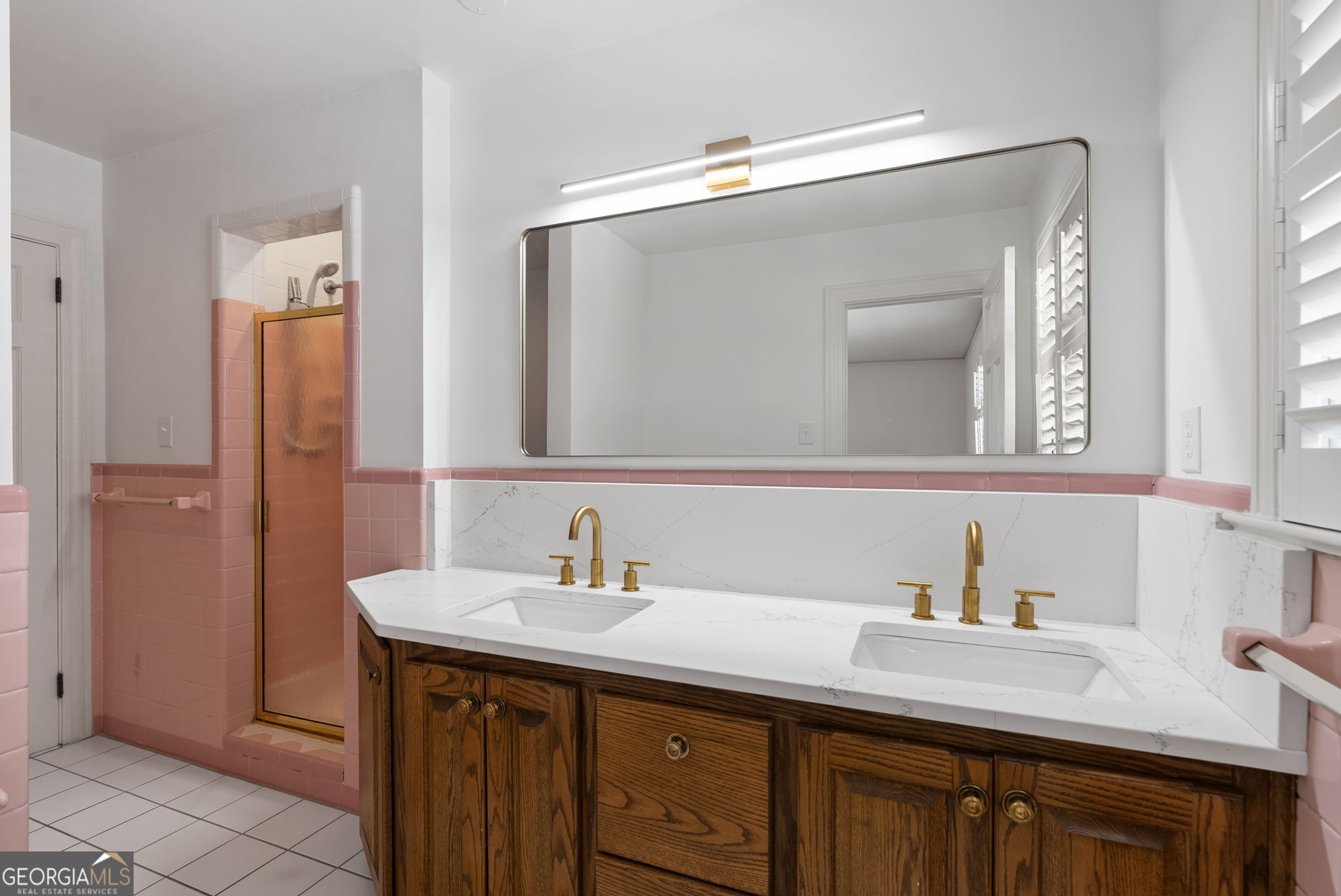 Bathroom with a double-sink wood vanity, brass faucets, pink tile, and a glass shower.