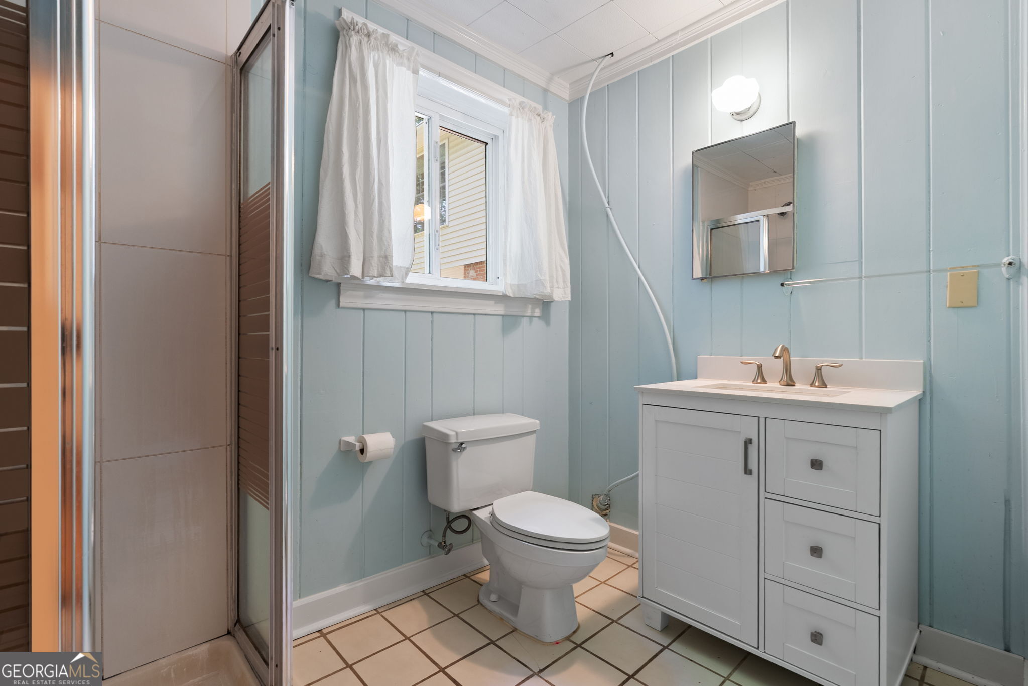 Bathroom with pale blue paneled walls, a white vanity, and a glass-enclosed shower.