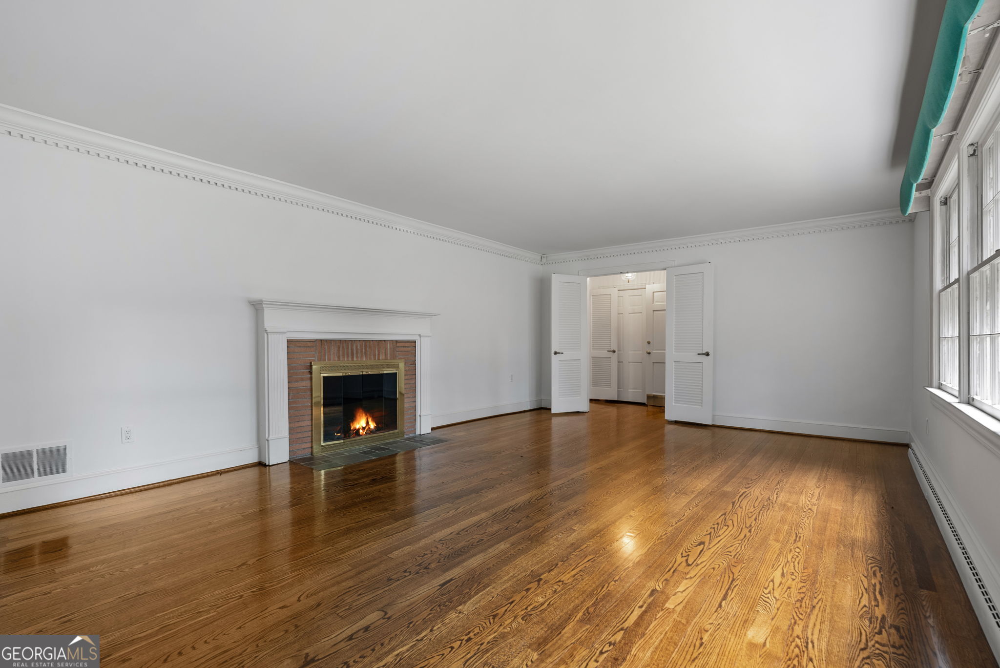 Empty living room with hardwood floors, a brick fireplace, and tall windows.