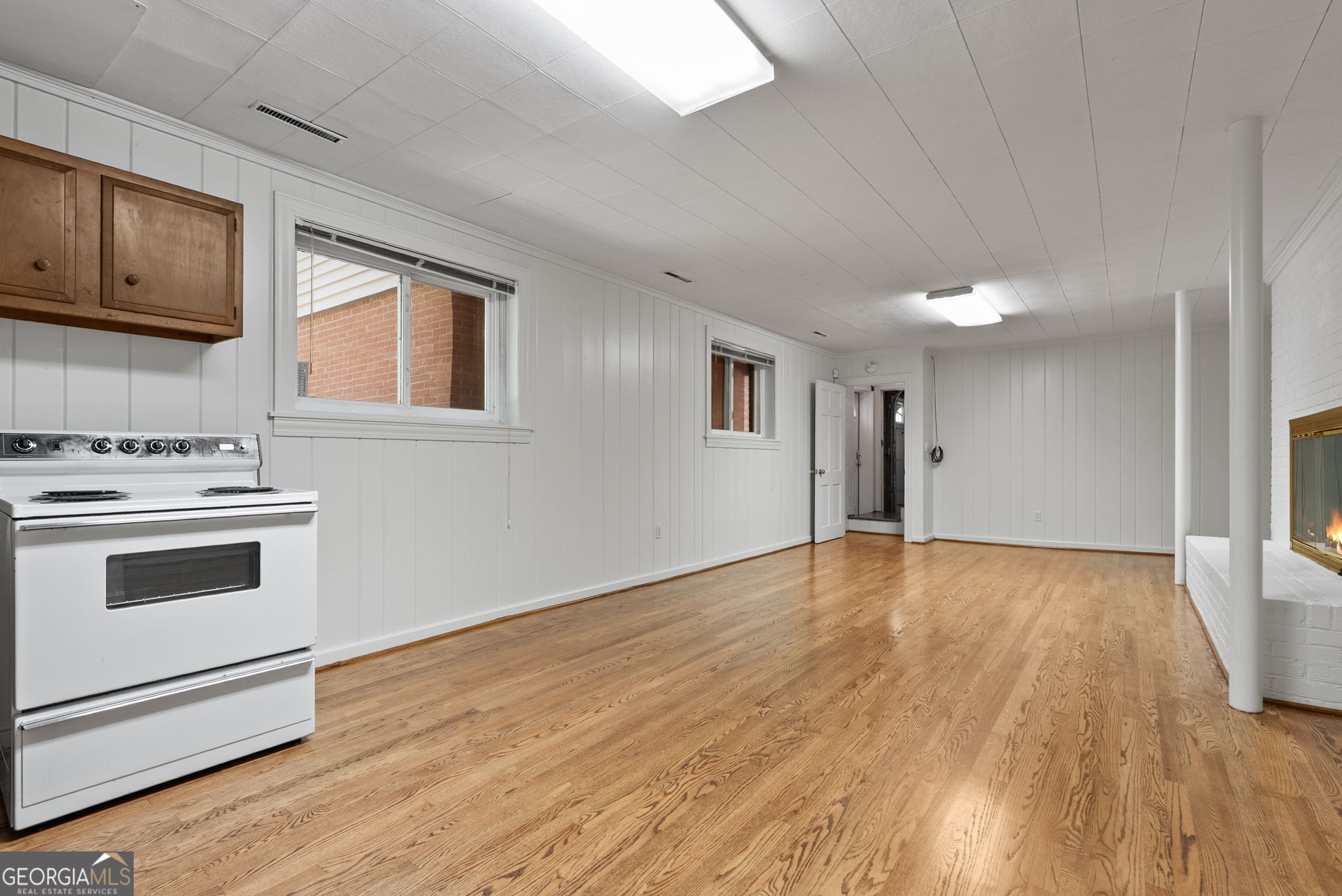 Unfurnished room with hardwood floors, a white stove, wooden cabinets, and a fireplace.