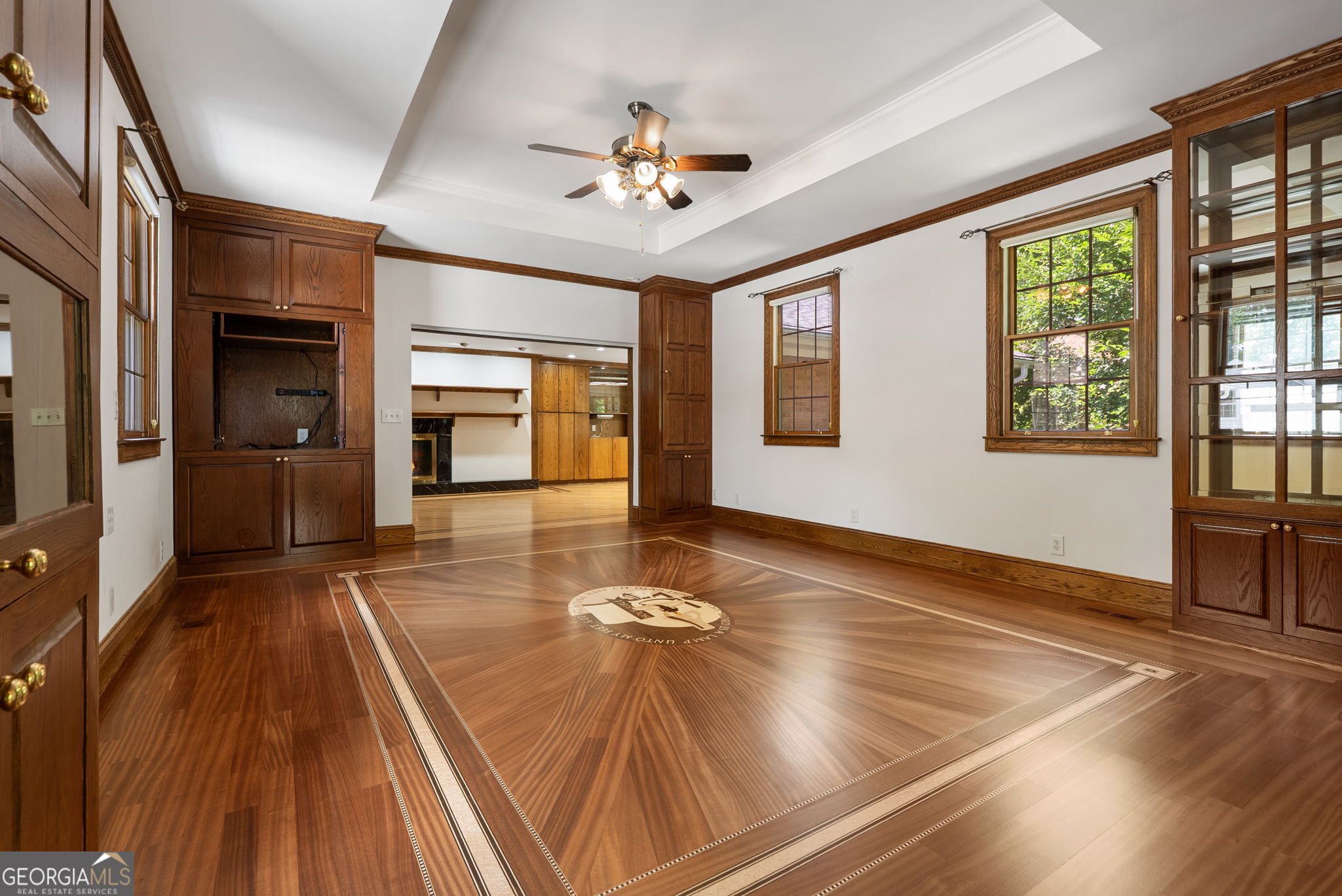Empty room with an ornate hardwood floor, dark wood built-ins, and a ceiling fan.