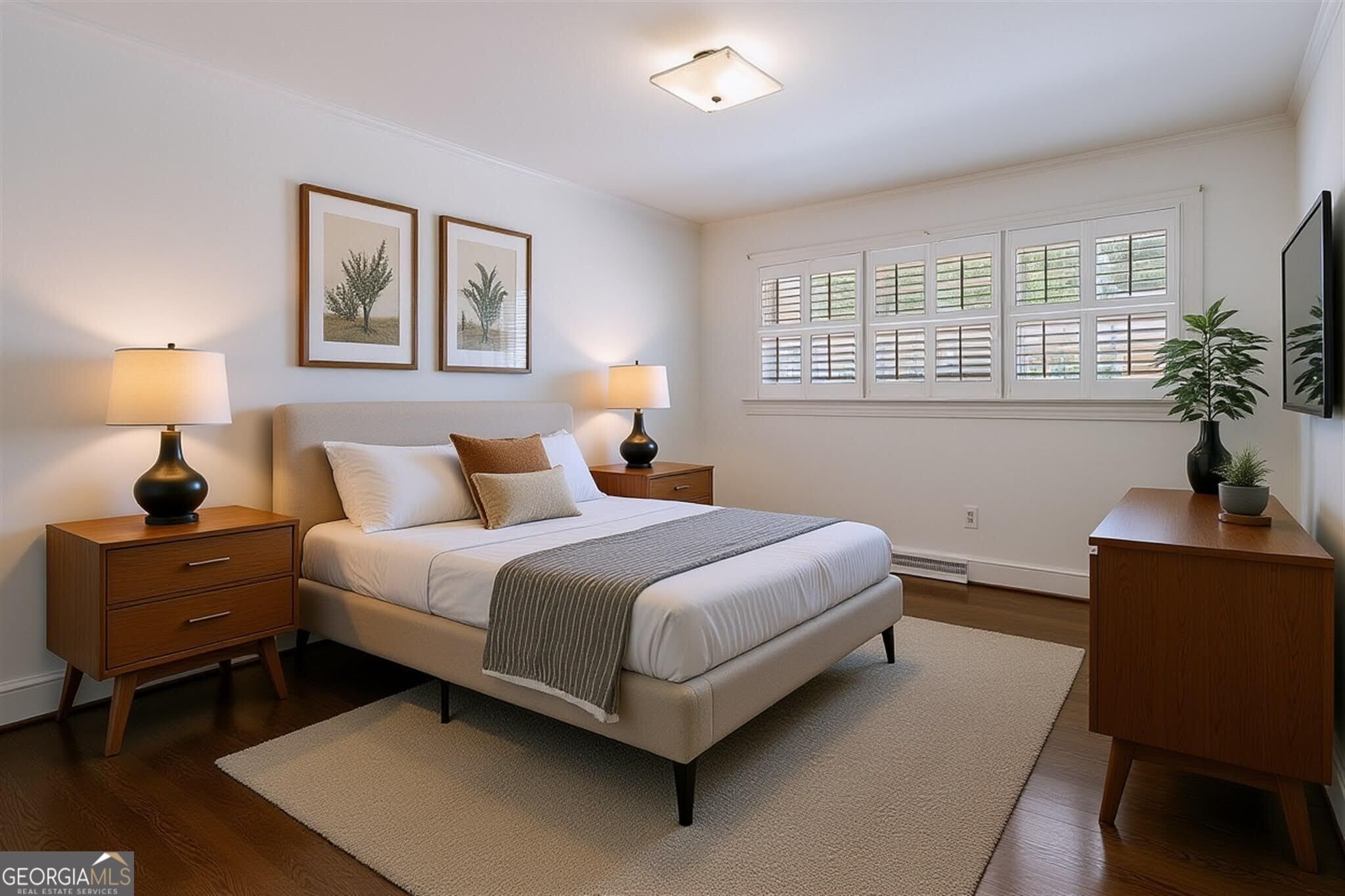 Staged bedroom with a neutral upholstered bed, warm wood furniture, and plantation shutters.