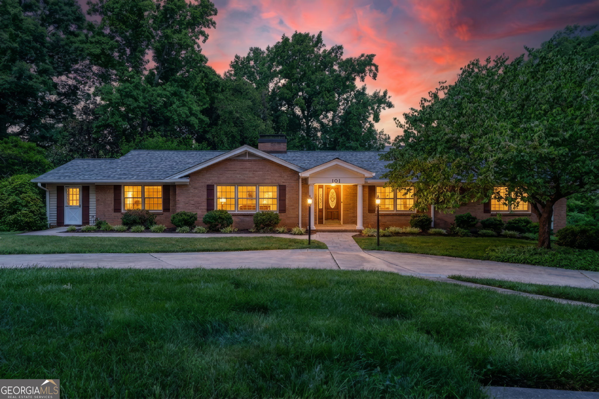 Brick ranch home with glowing windows and a covered entry beneath a vivid dusk sky.