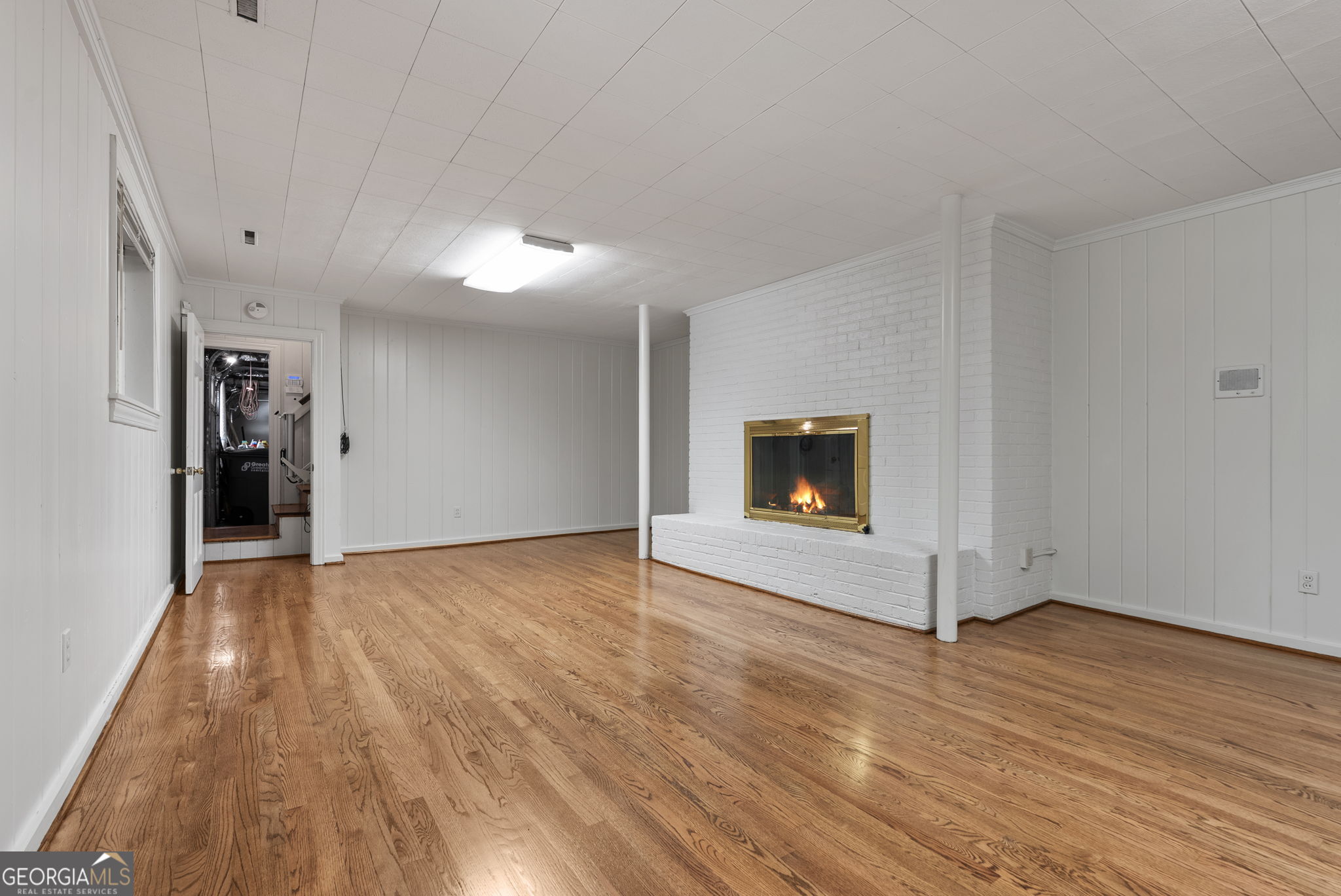 Empty room with hardwood floors and a white brick fireplace.