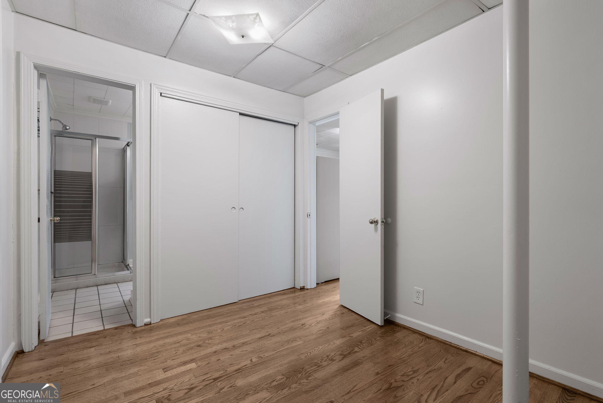 Empty room with hardwood floors, a sliding-door closet, and an adjoining tiled bathroom.