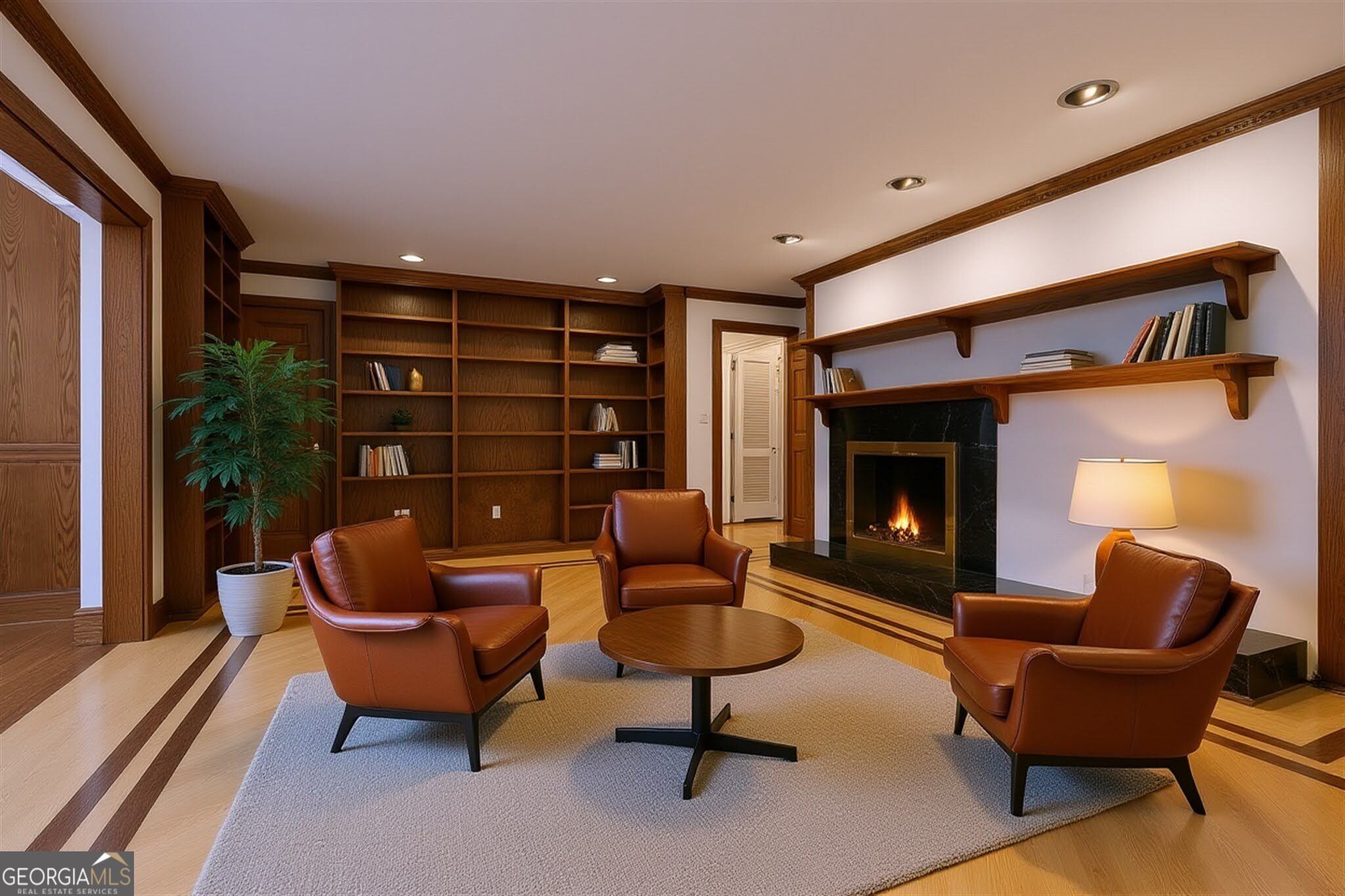 Furnished study with built-in wood bookshelves, leather armchairs, and a lit fireplace.