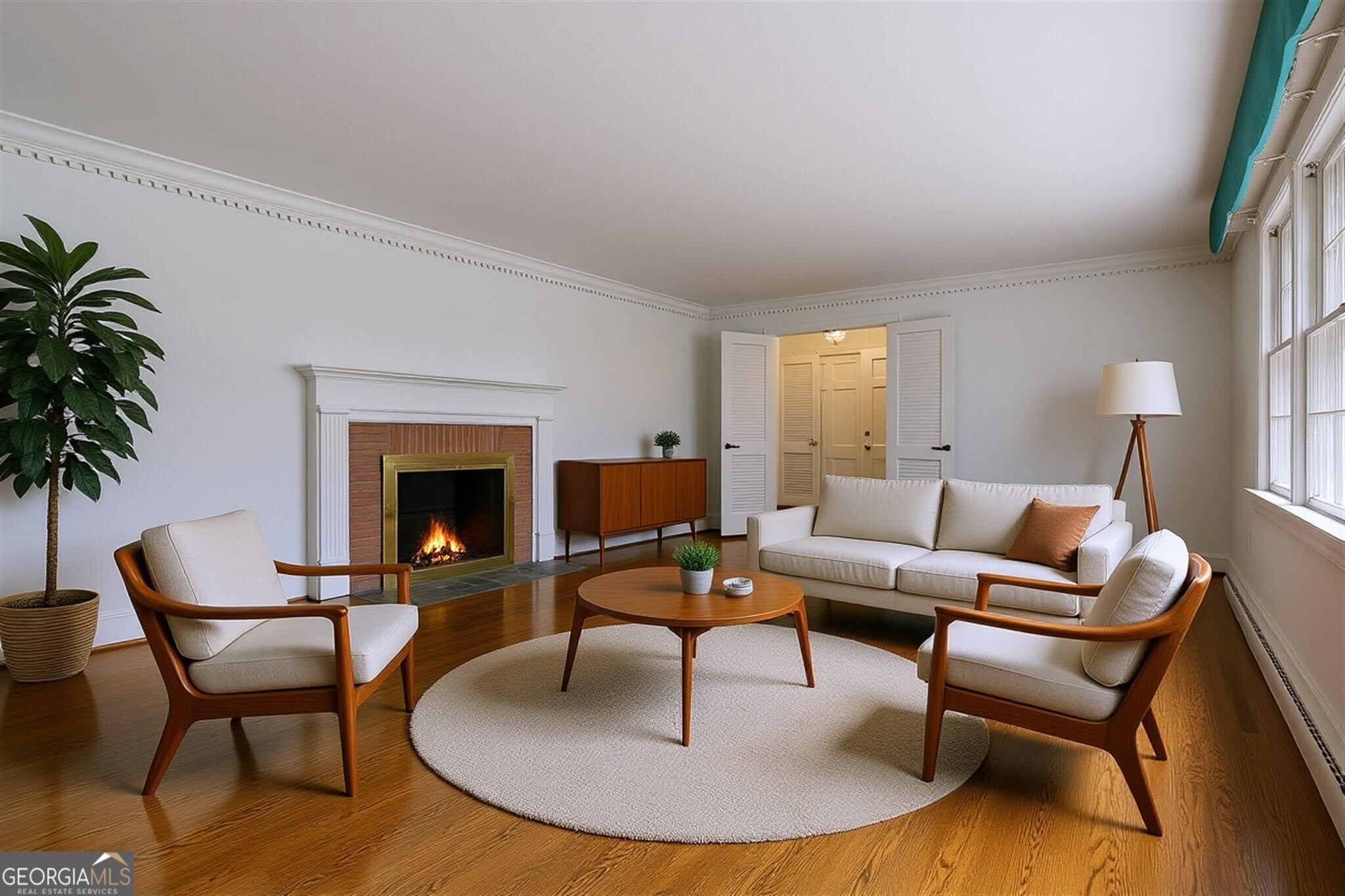 Staged living room with a brick fireplace, hardwood floors, and large windows.