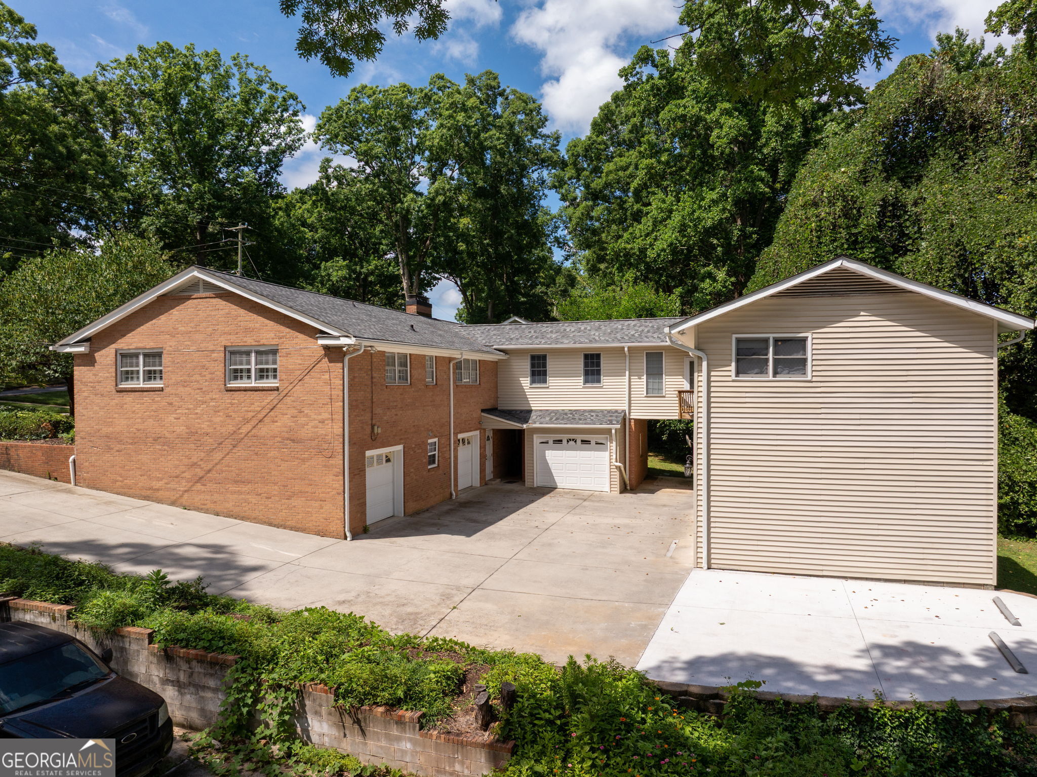 Two-story brick and beige-sided home with multiple garages and a broad driveway beneath mature trees.