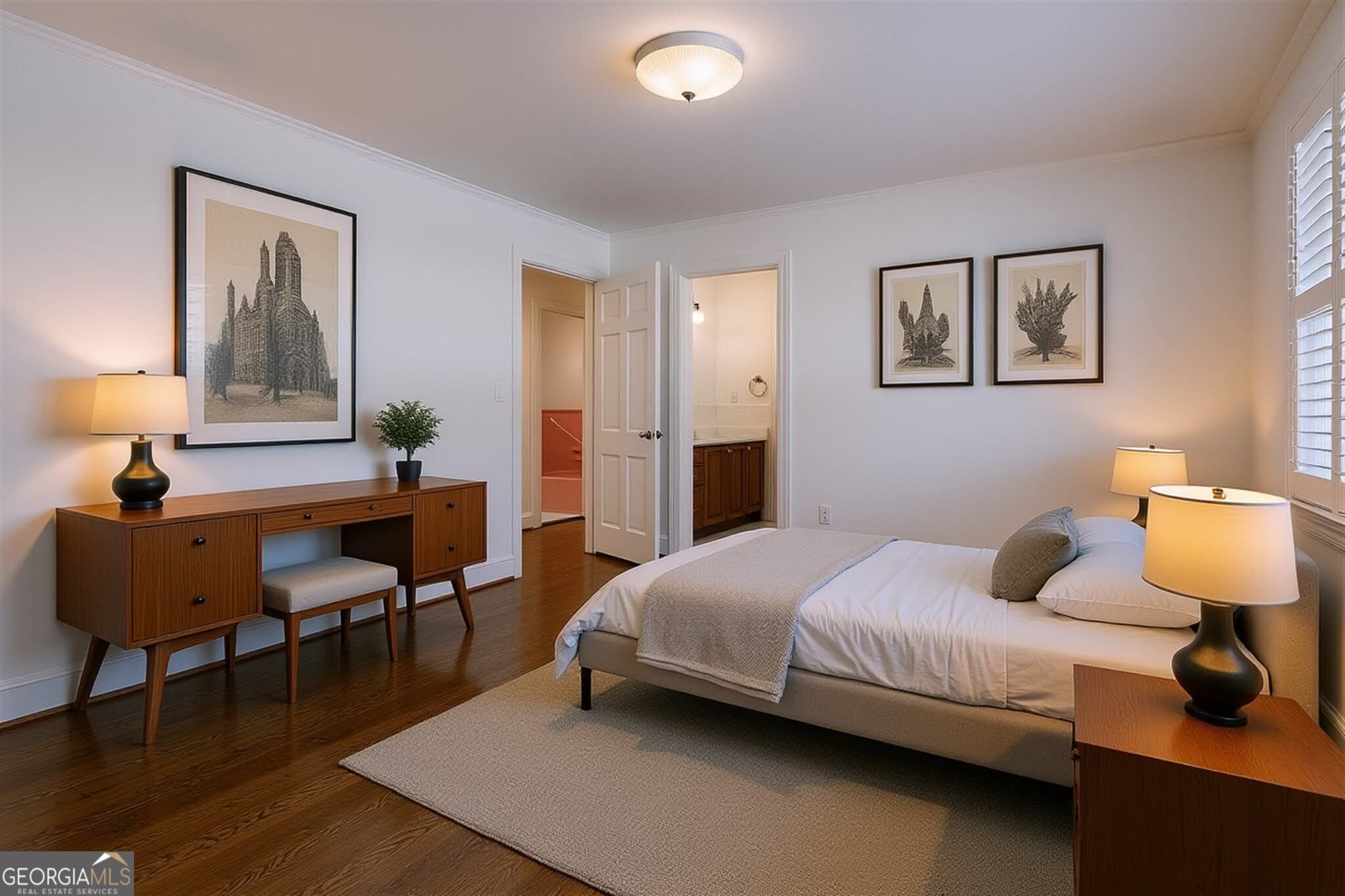 Bedroom with a white bed, dark wood floors, botanical prints, and a matching wooden desk.