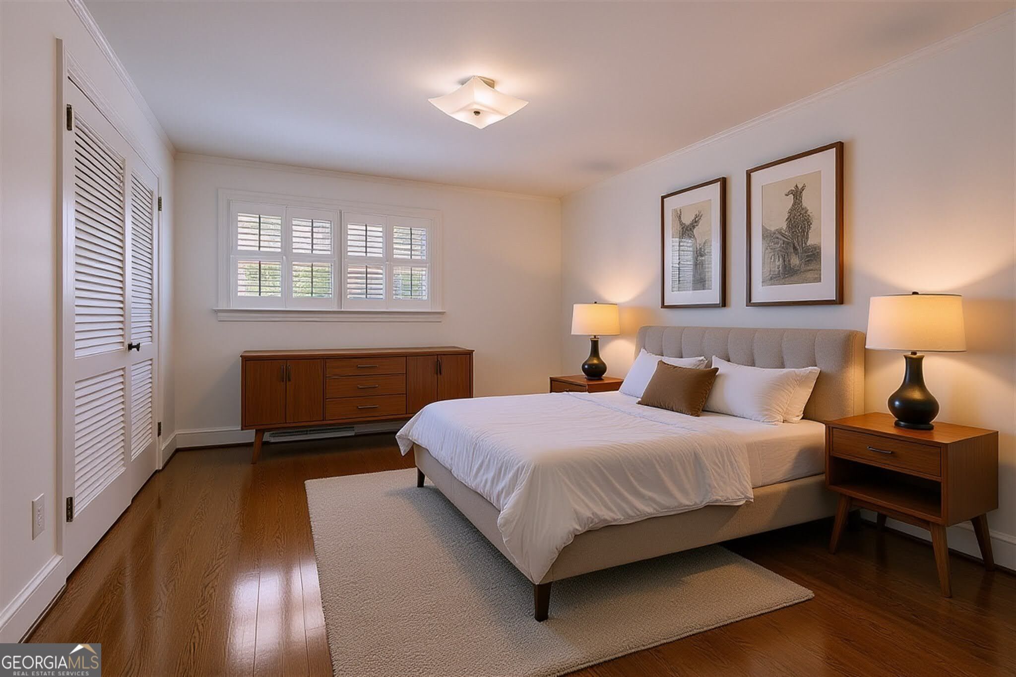 Furnished bedroom with a large upholstered bed, hardwood floors, and plantation shutters.