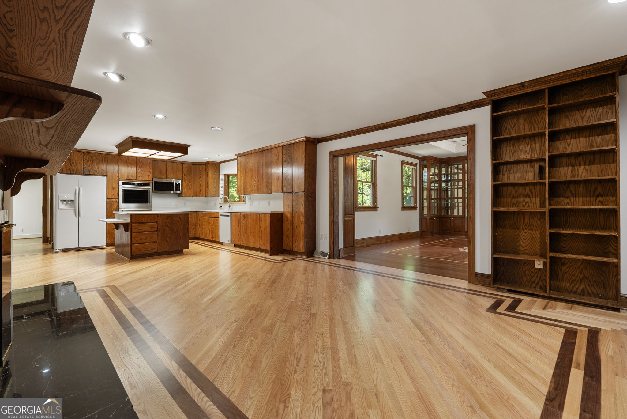 Kitchen with wood cabinetry, stainless steel appliances, hardwood floors, and built-in bookshelves.