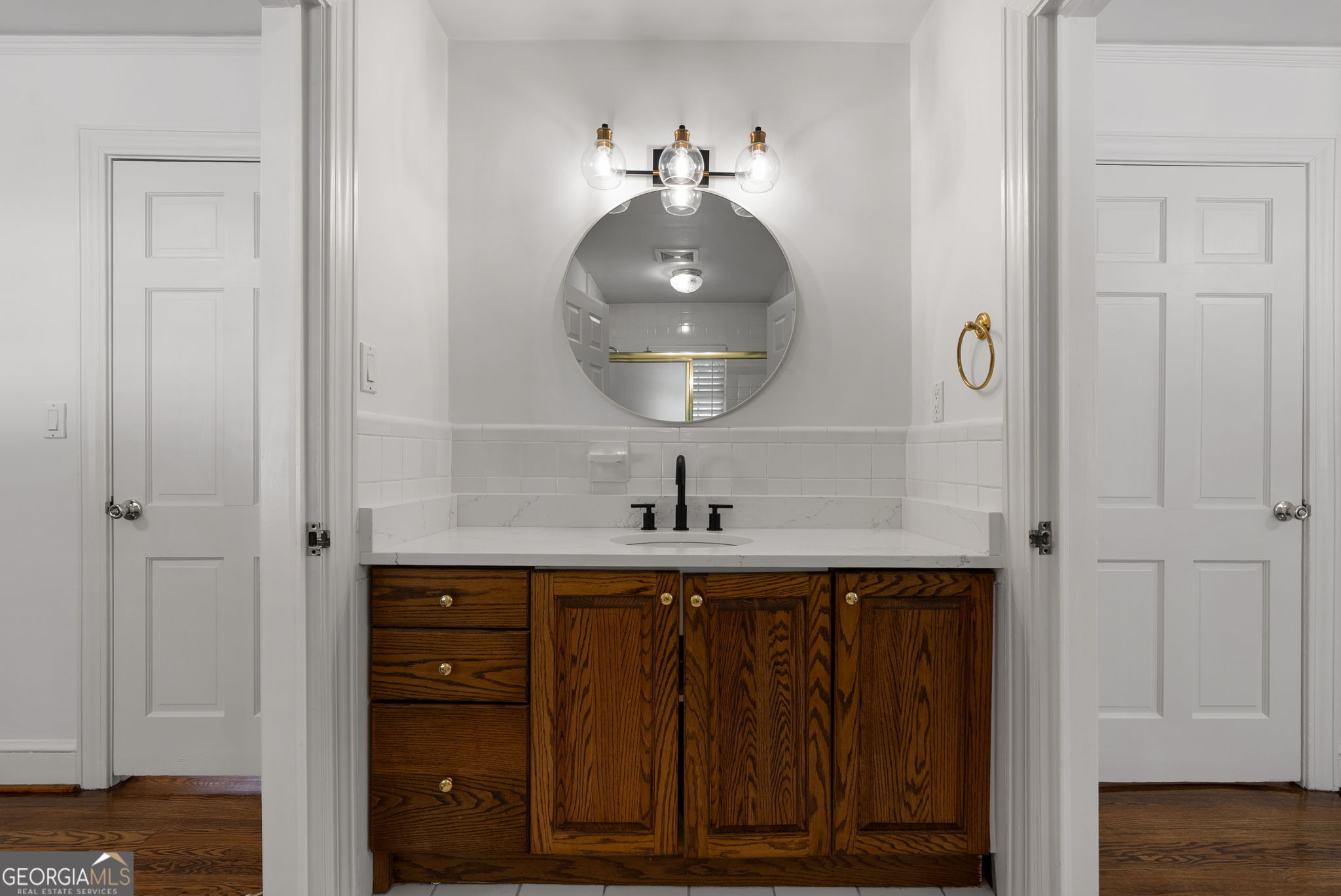 Bathroom vanity with dark wood cabinetry, a white countertop, round mirror, and black faucet.