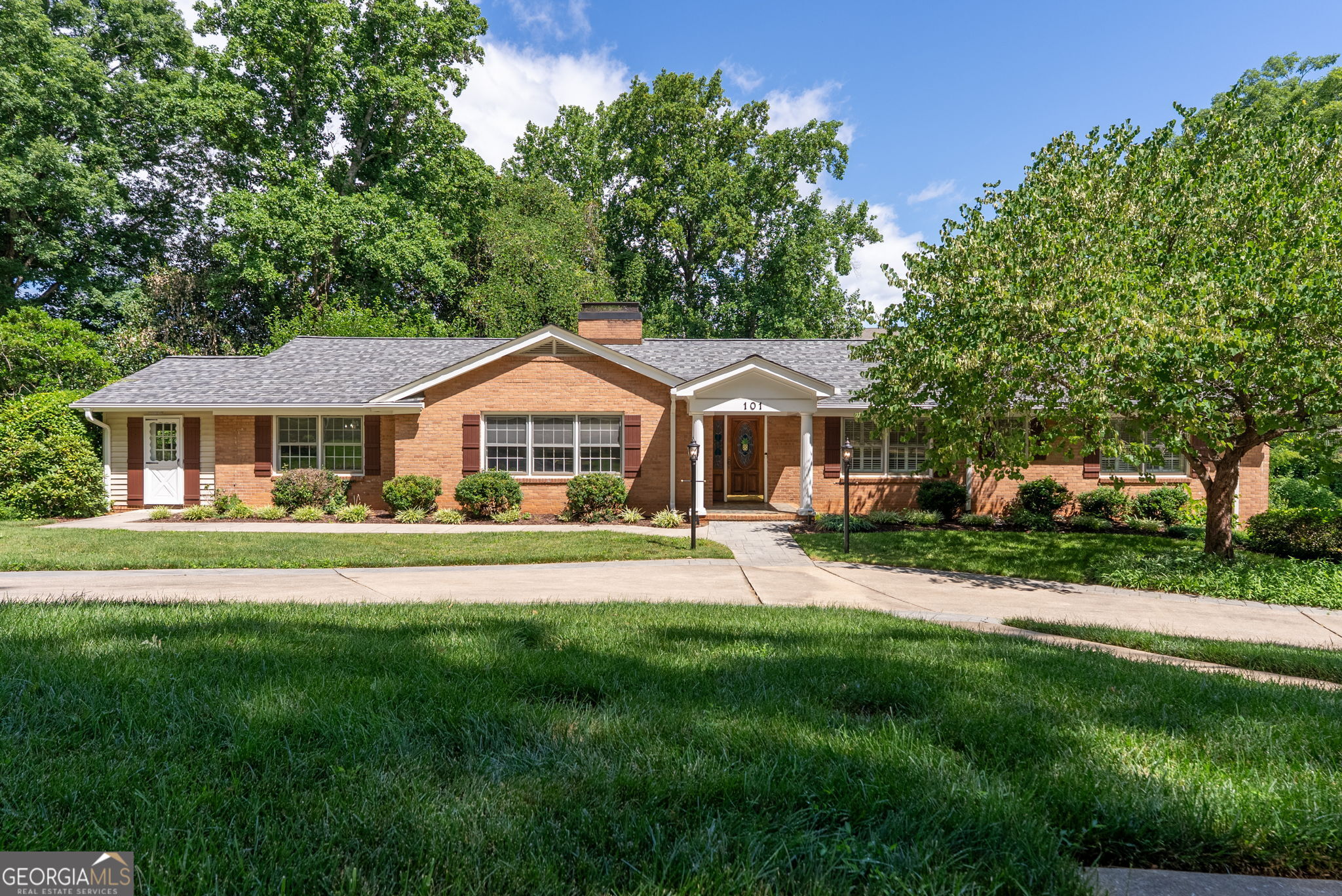 Single-story brick home with a white entrance portico, landscaped shrubs, and broad front lawn.