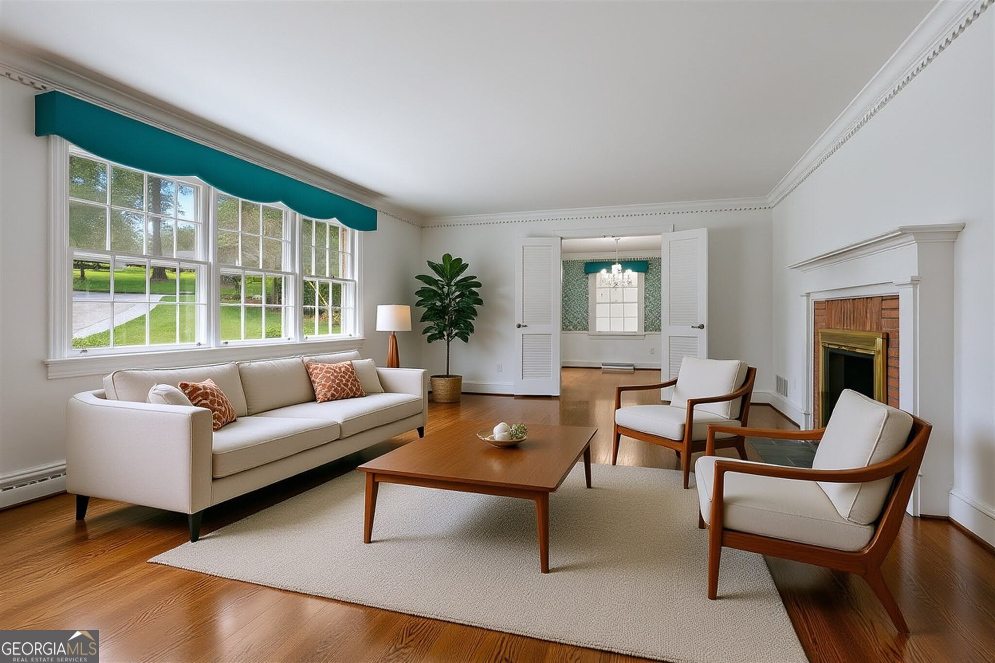 Living room with large windows, a cream sofa, wood-framed chairs, and a brick fireplace.