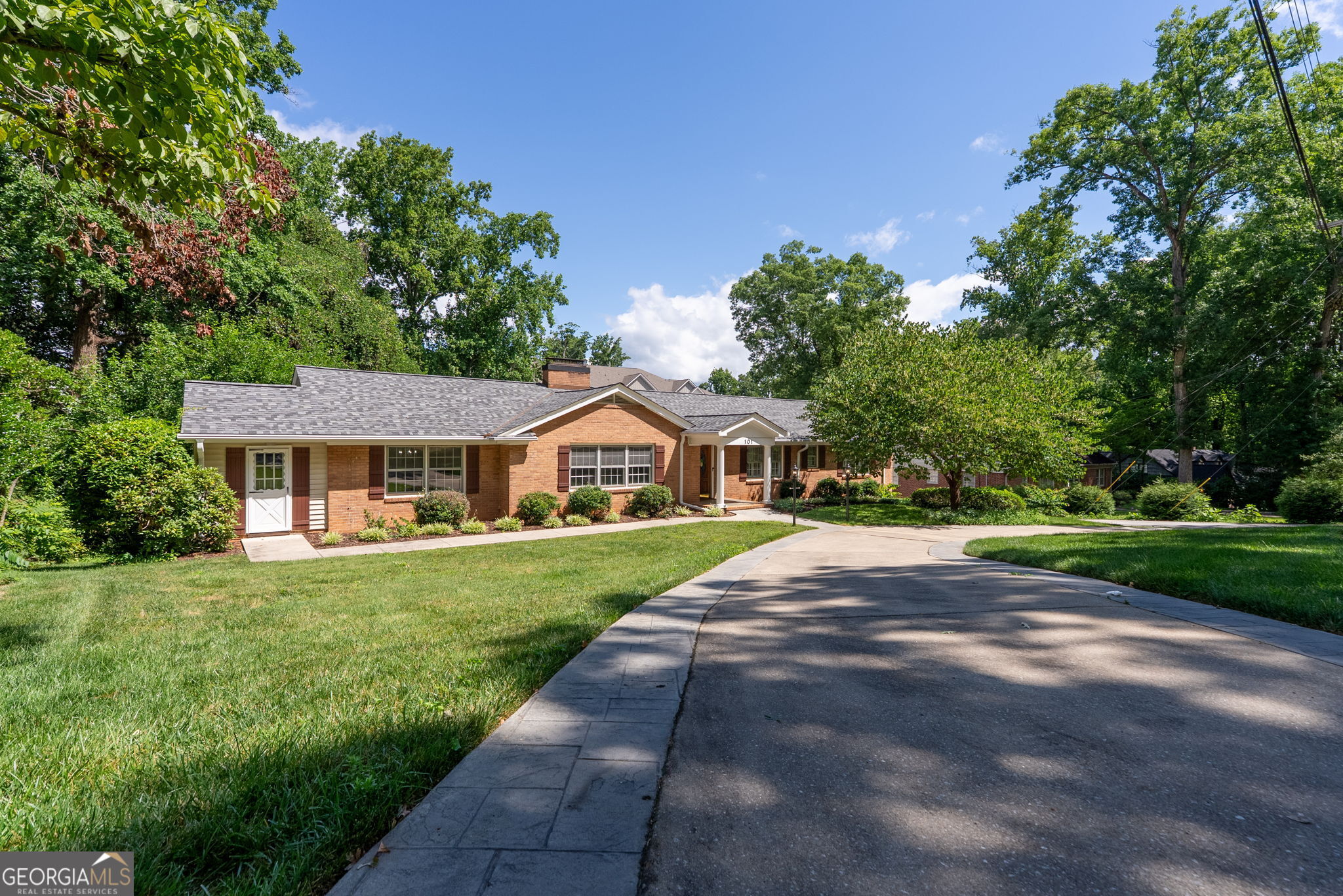 Single-story brick home with a white entry portico, landscaped lawn, and curved driveway.