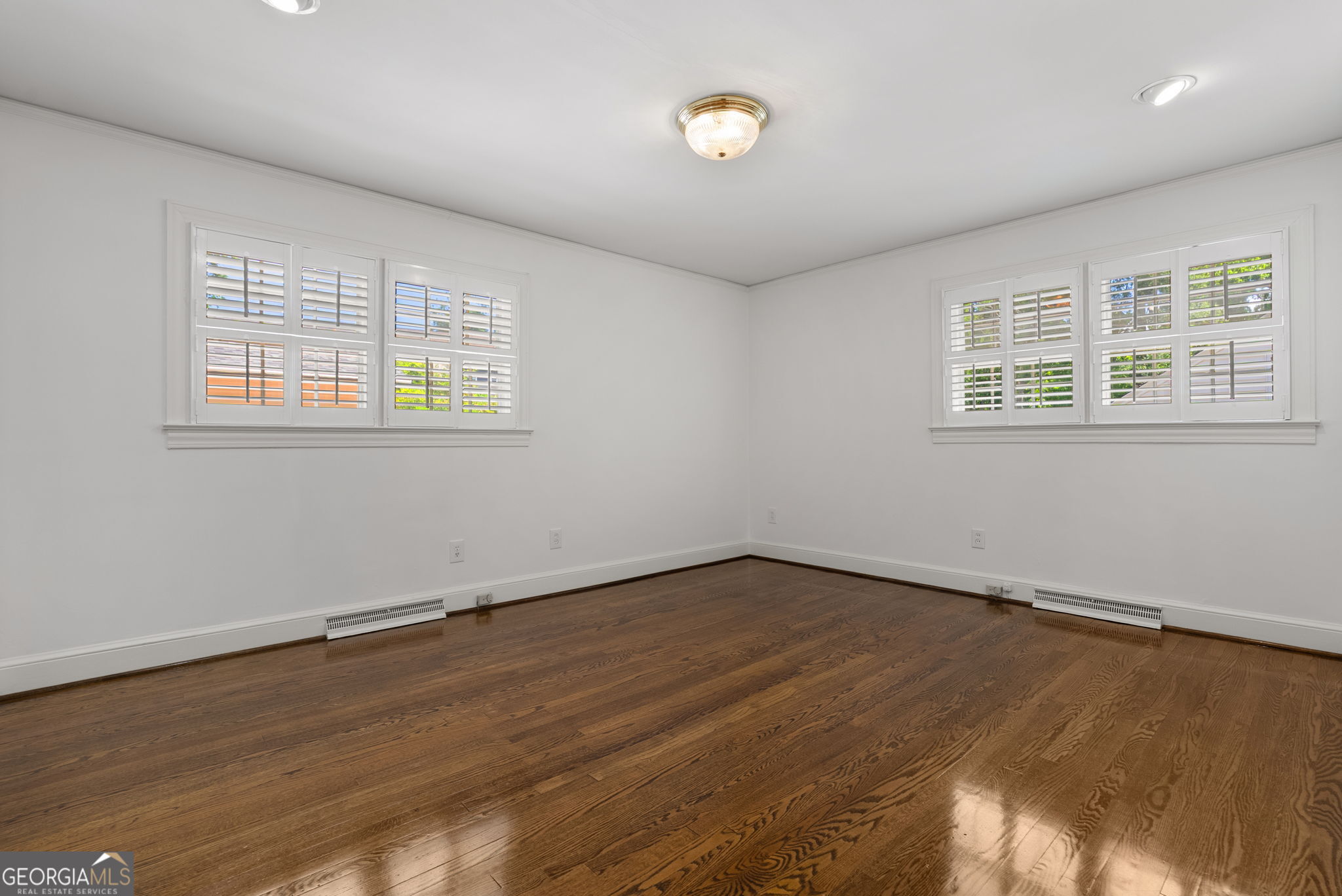 Empty room with polished hardwood floors and plantation-shuttered windows.