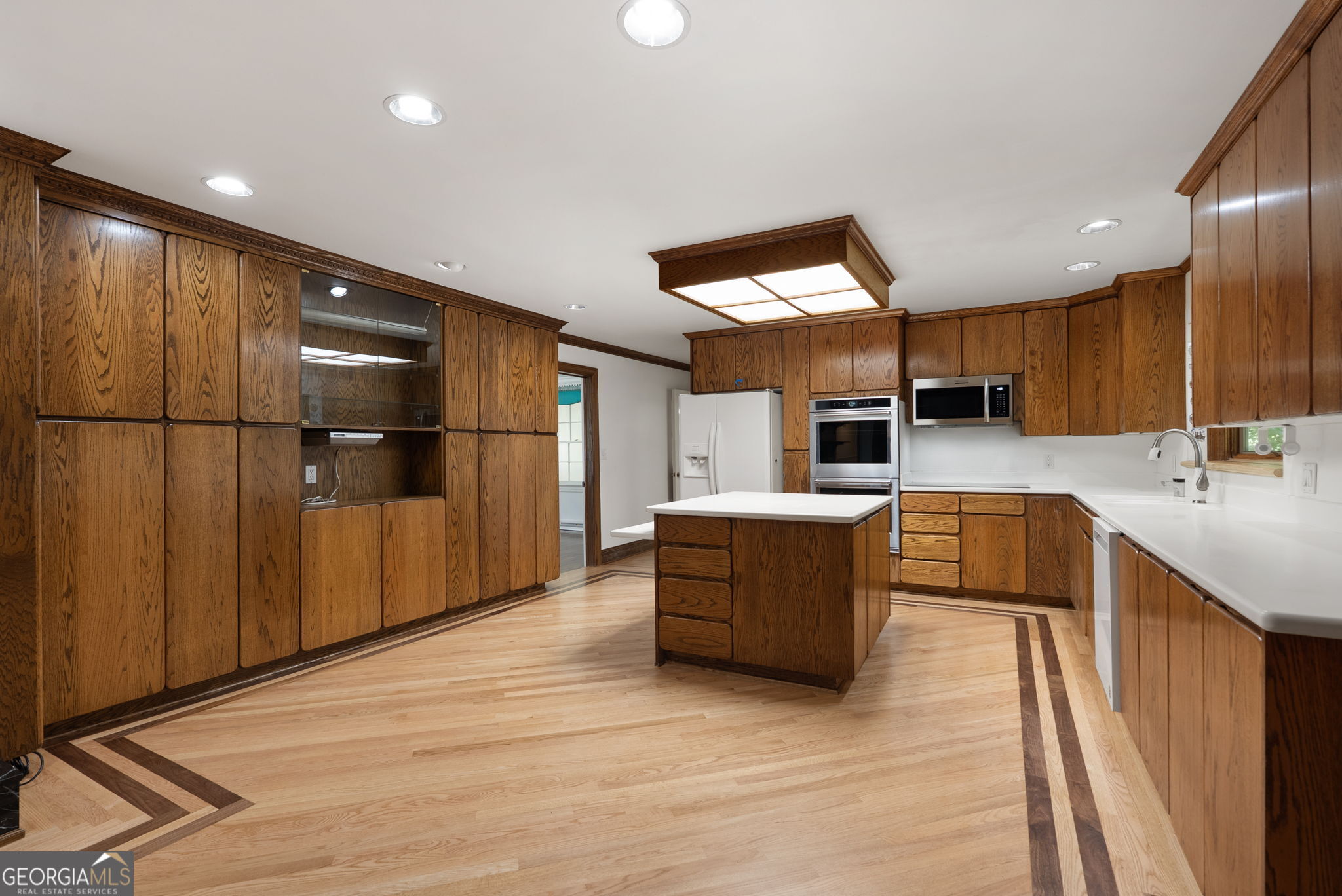 Kitchen with extensive wood cabinetry, white countertops, a central island, and light wood flooring.