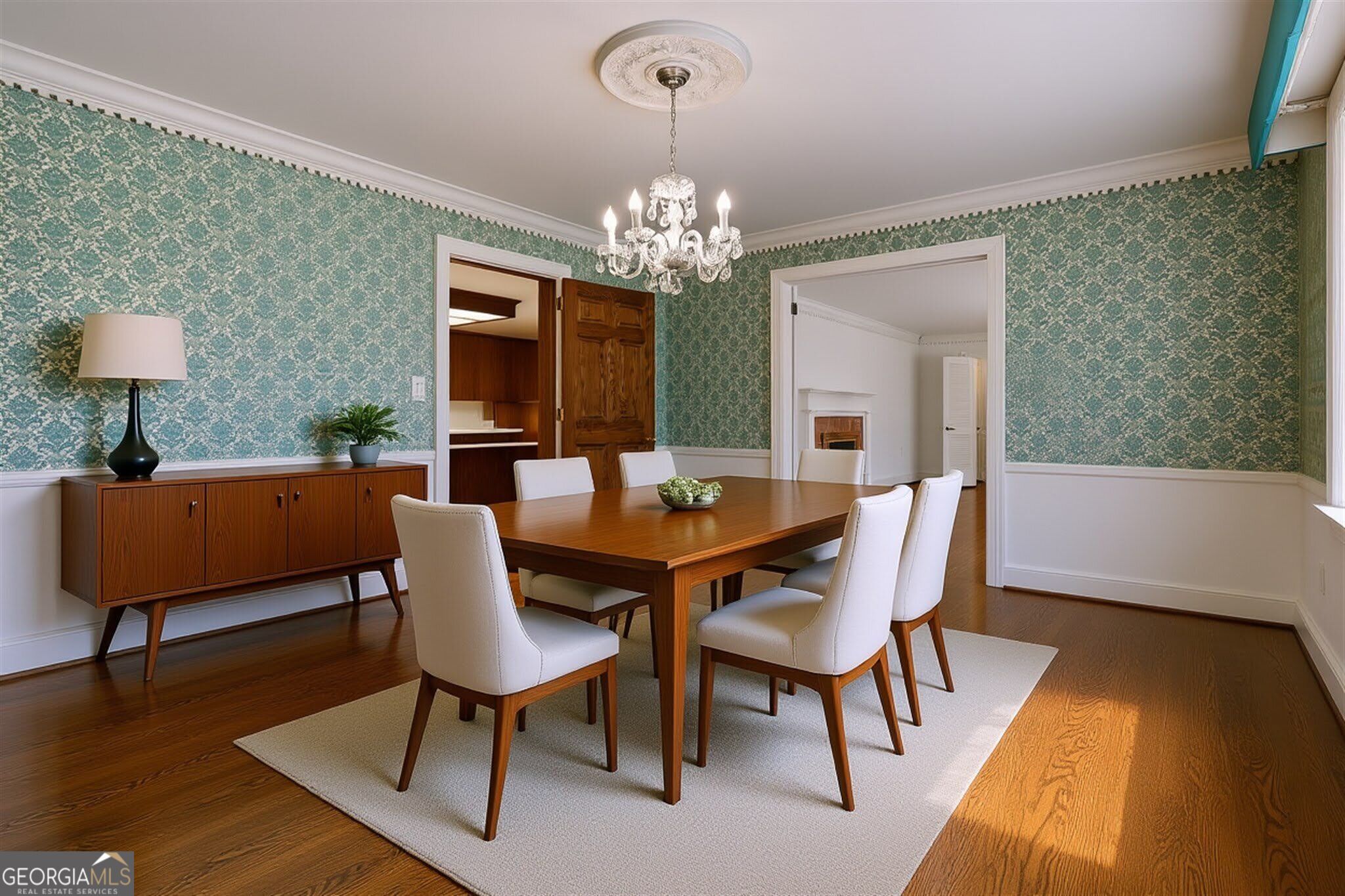 Furnished dining room with green patterned wallpaper, a crystal chandelier, and a wood dining table.
