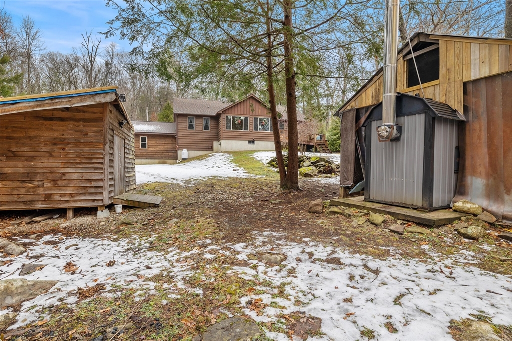 Brown house viewed between two wooden outbuildings in a snowy, wooded yard.