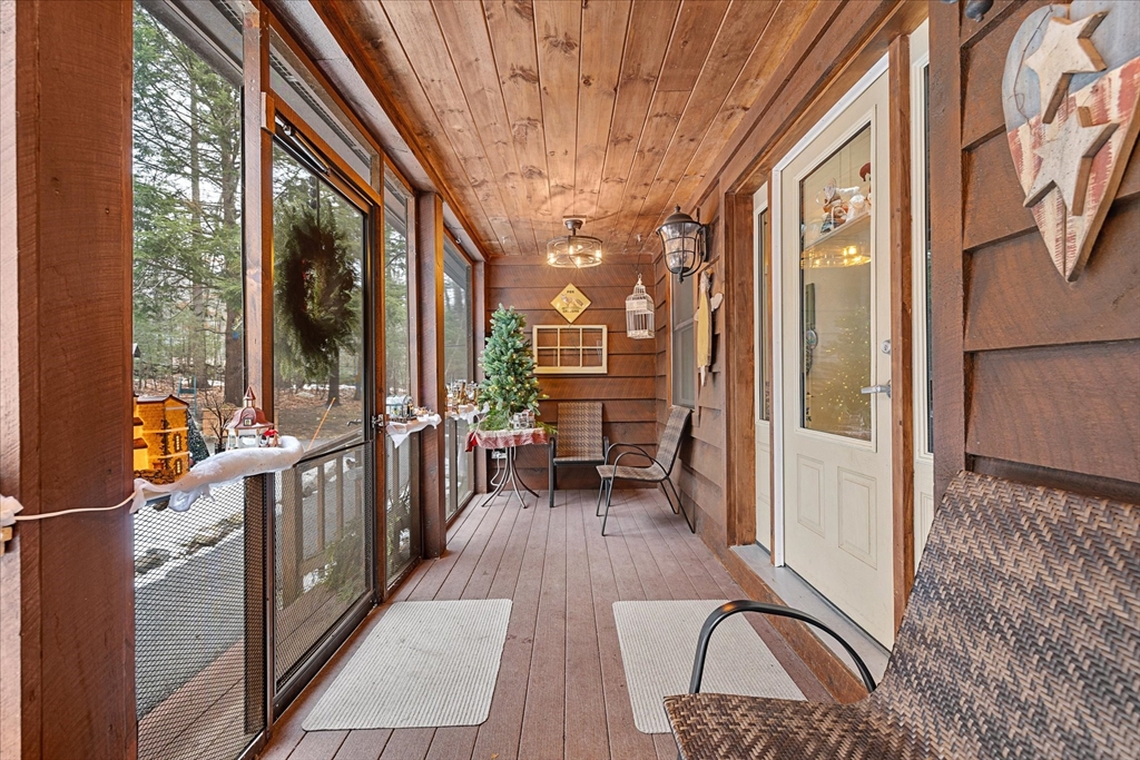 Enclosed wood-paneled porch with screened windows, wicker chairs, and a small Christmas tree.