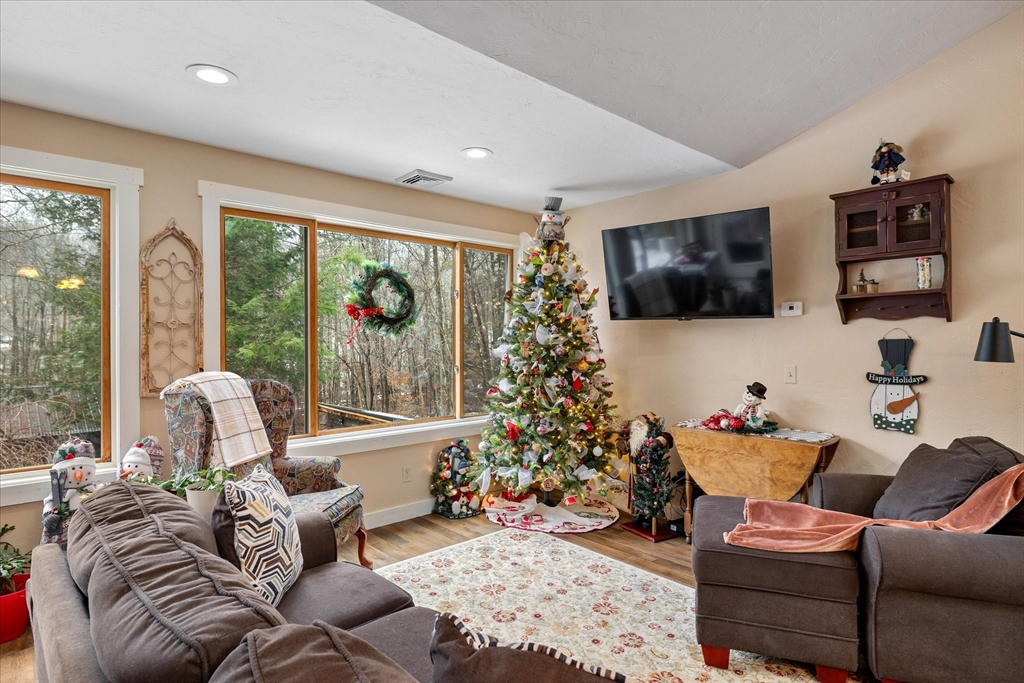 Furnished living room with a Christmas tree and large windows overlooking the woods.
