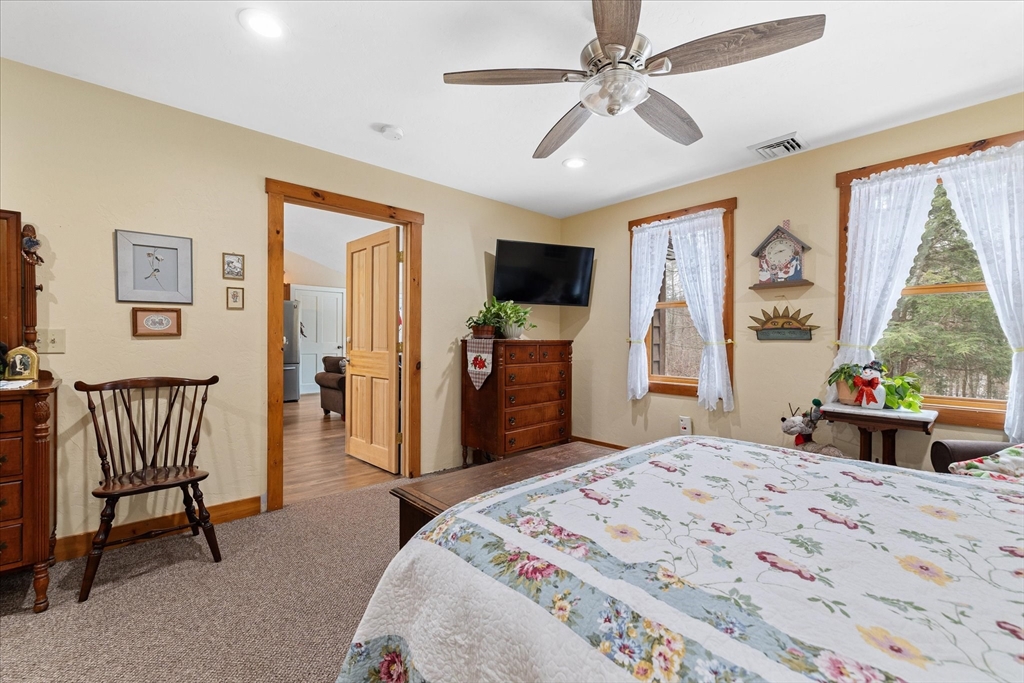 Bedroom with a floral quilt and wood-trimmed windows overlooking trees.