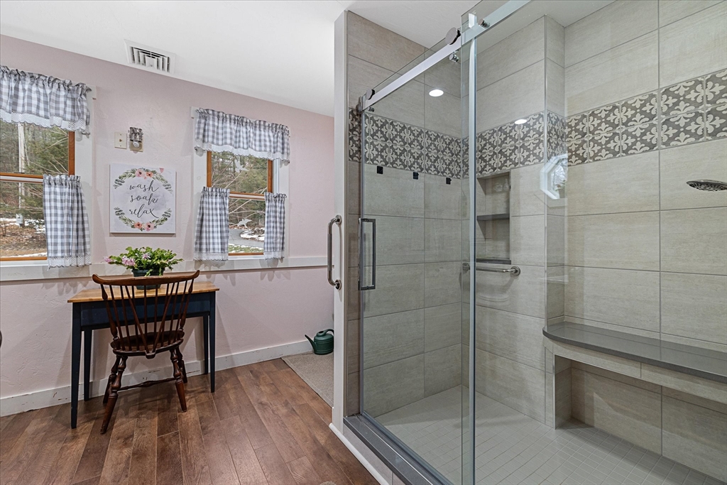 Bathroom with a glass-enclosed tiled shower, patterned tile band, and built-in bench beside two curtained windows.