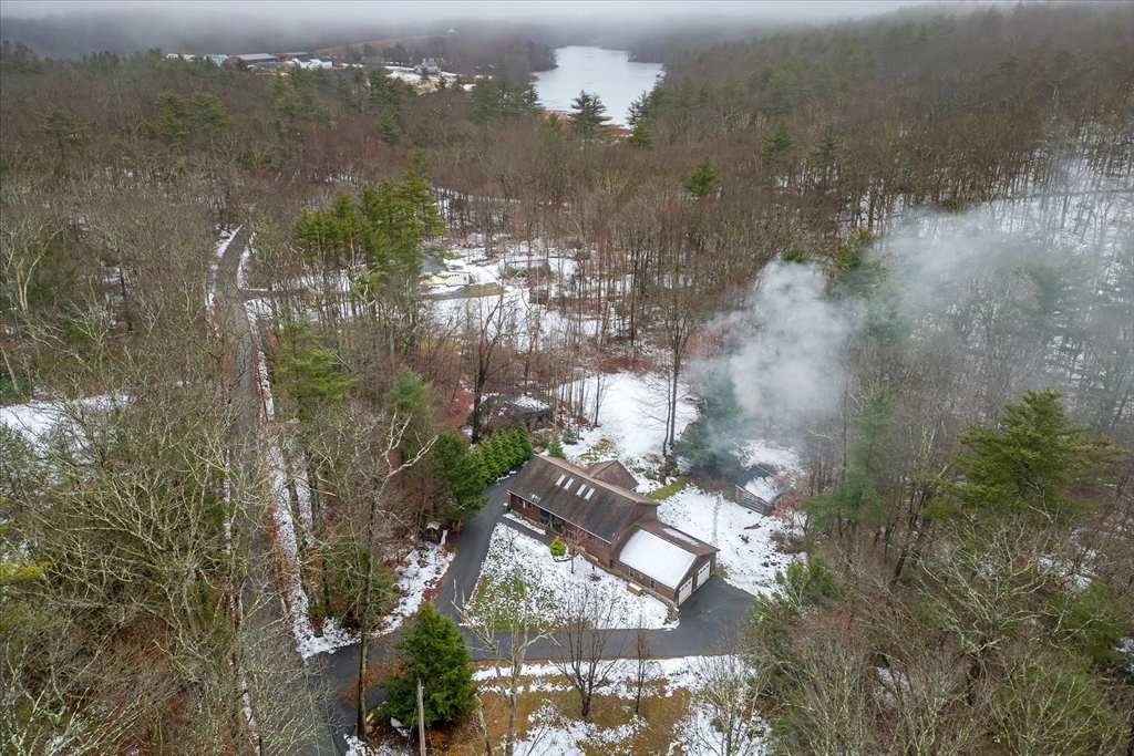 Aerial view of a wooded home in winter, with a lake visible beyond the snow-covered grounds.