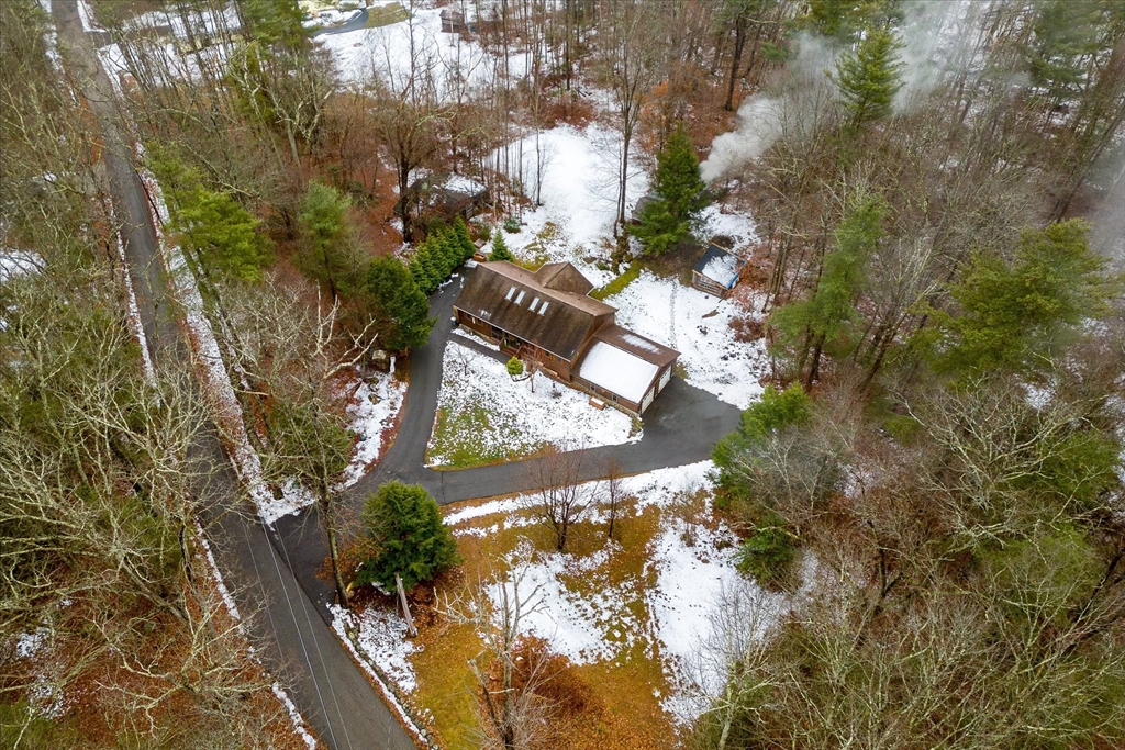 Aerial view of a wooded property with a looping driveway and patchy snow.