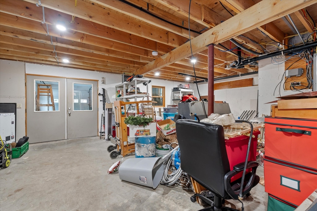 Unfinished basement with exposed ceiling joists, concrete floor, and crowded storage and equipment.