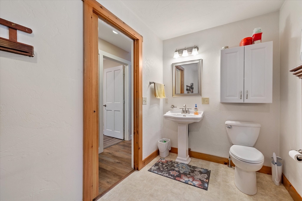 Bathroom with a pedestal sink, wall cabinet, and patterned rug beside a wood-trimmed doorway.