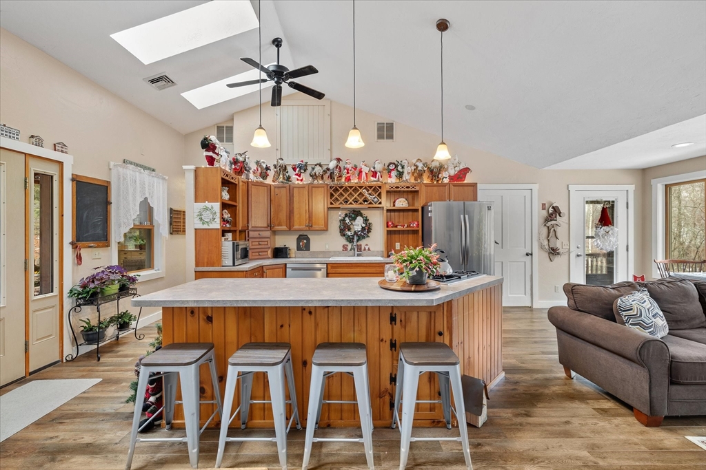 Open-plan kitchen with a large wood island, metal stools, warm cabinetry, and vaulted skylit ceiling.