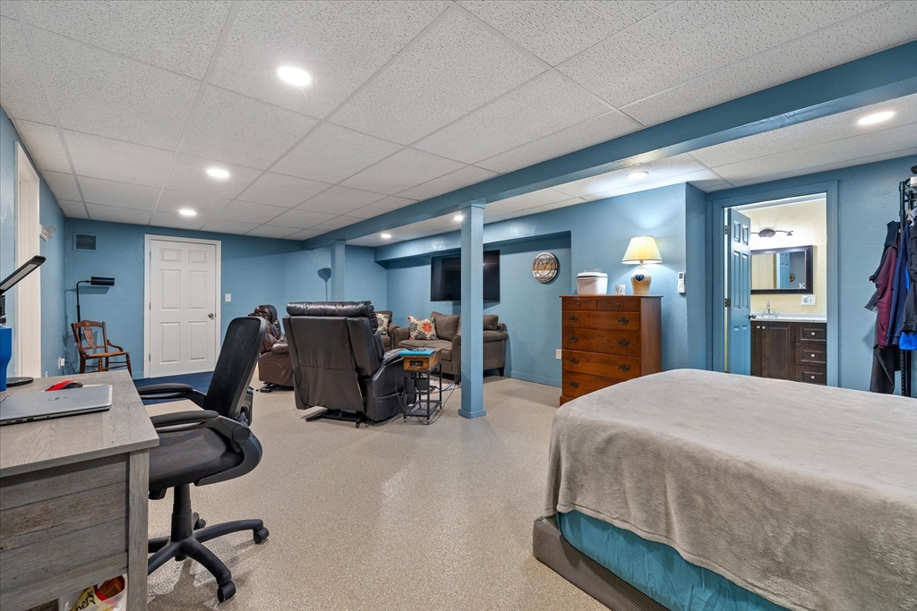 Furnished basement room with a bed, recliners, television, desk, and adjoining bathroom.