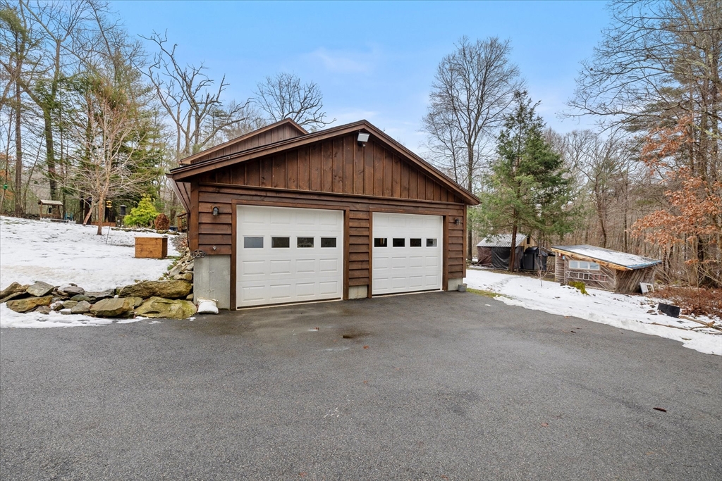 Detached wood-sided garage with two white doors beside a snowy driveway.