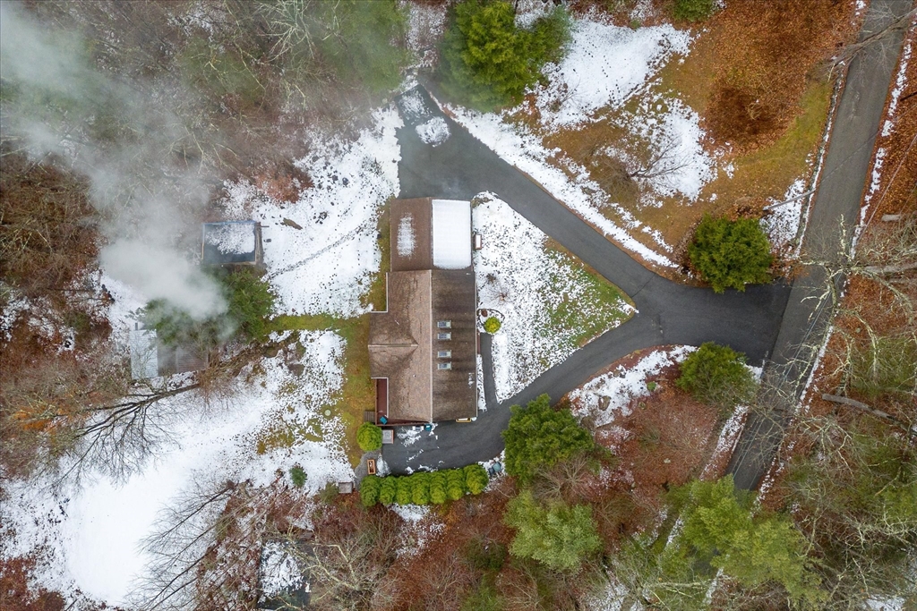 Aerial view of a house and branching driveway amid patchy snow and leafless woods.