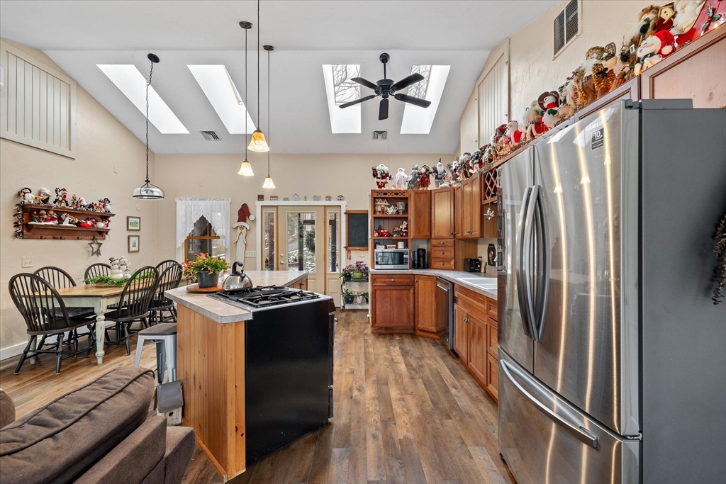 Kitchen with skylights, a central cooktop island, wood cabinetry, and a dining table.