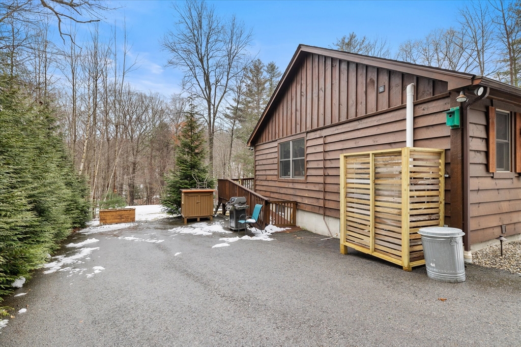 Brown-sided house beside a paved patio with a wooden privacy screen and snow-dusted wooded yard.