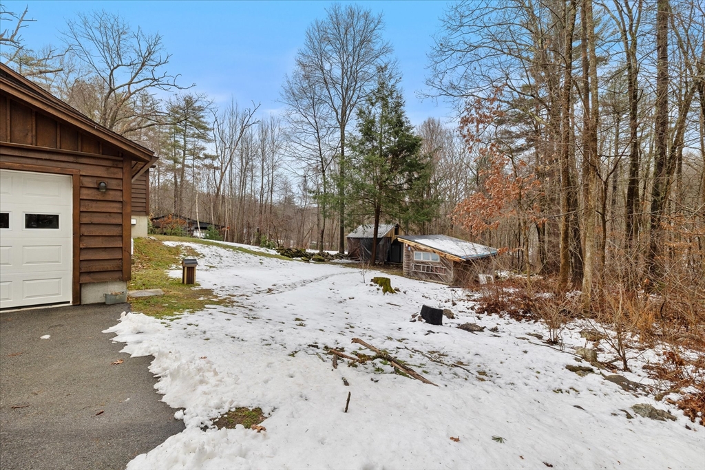 Snow-covered yard beside a wood-sided home, with a white garage door and outbuildings.